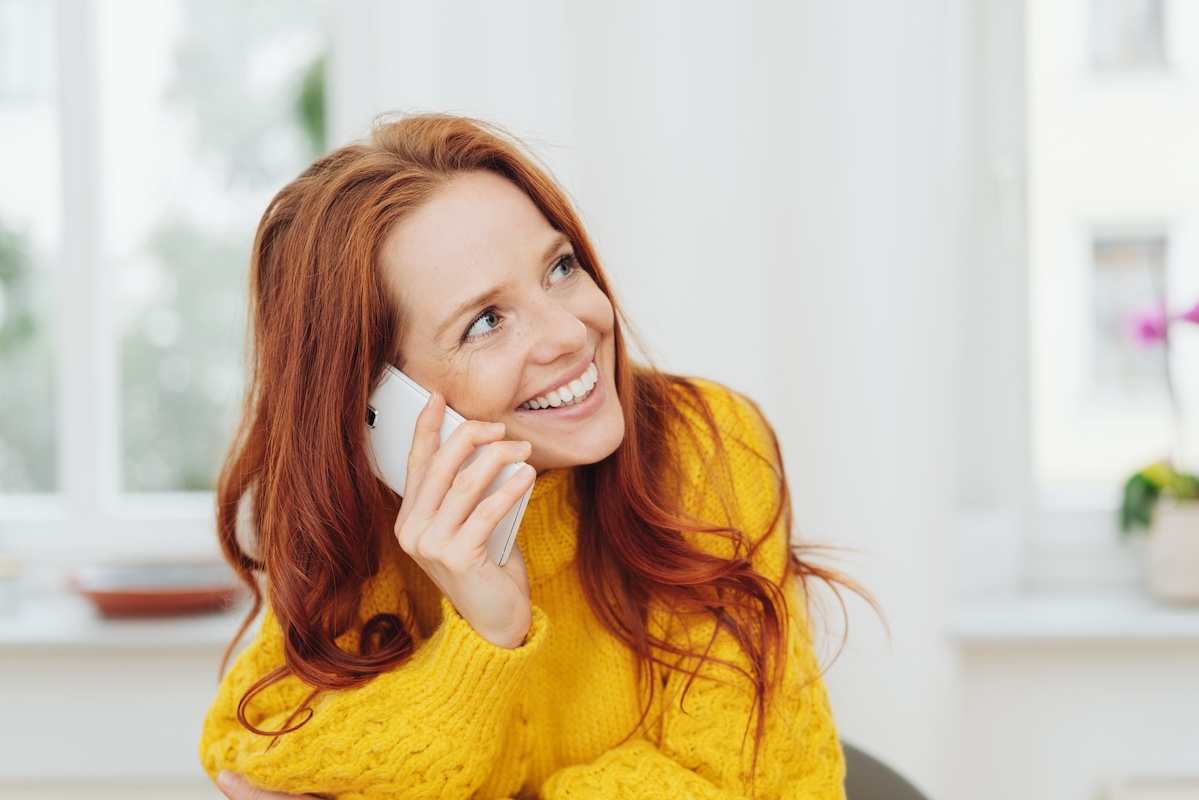 Portrait of smiling red-haired woman wearing yellow sweater talking on phone
